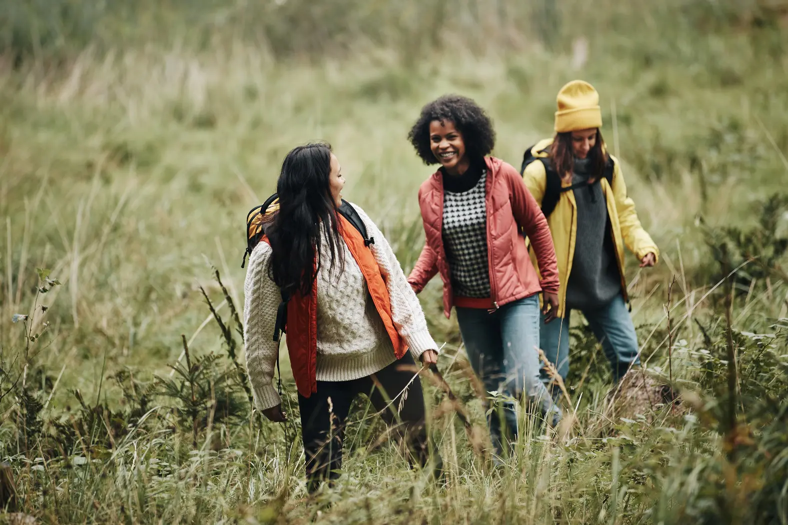 Three friends happily walk through a grassy field on a hike.