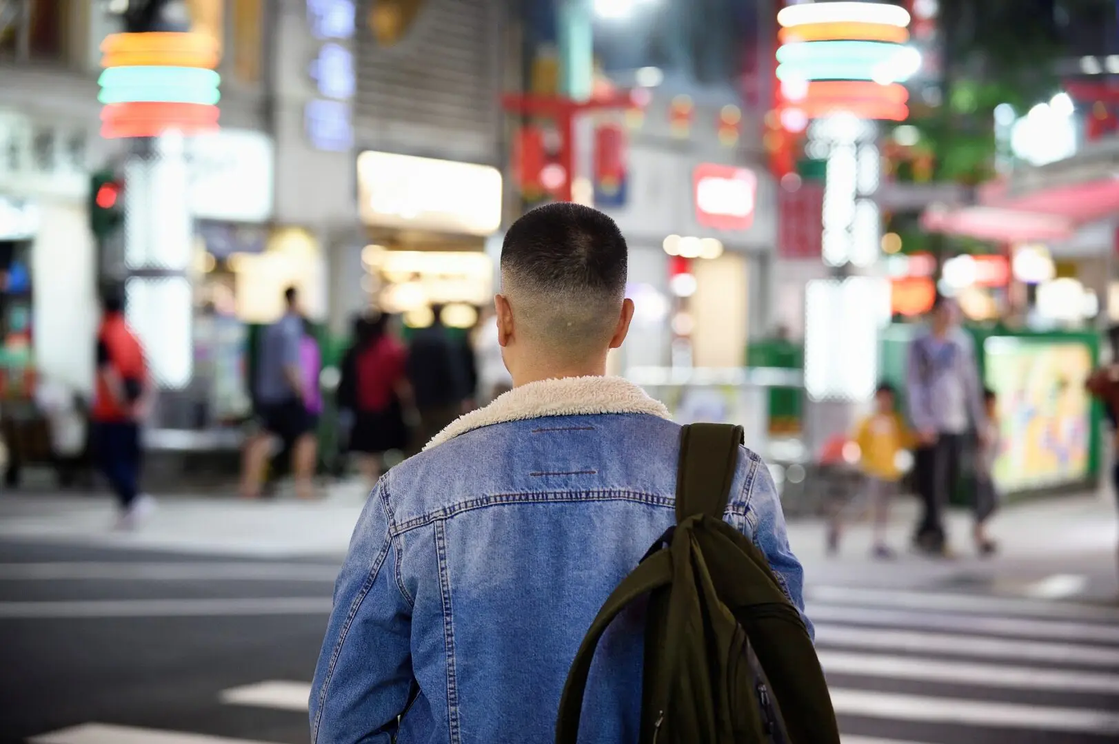 Person standing on a busy city street at night with a backpack.