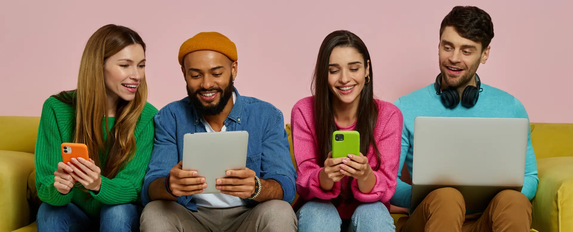 Two friends happily using their devices together against a pink background.