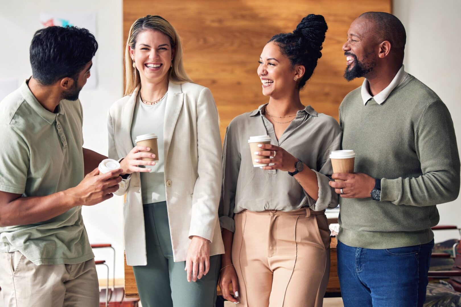Four colleagues enjoying coffee and chatting in a casual office setting.